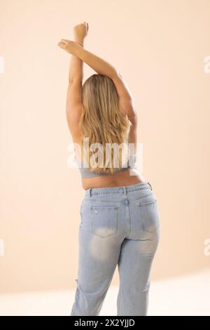 Kaukasische, junge Frau in Übergröße, die sich in Casuals ausdehnt, beige Kulisse Stockfoto