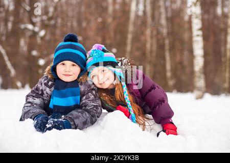 Kleine Mädchen und Junge liegen in der Nähe auf der Schneelage im Winterpark Stockfoto