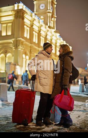 Junger Mann und junge Frau stehen am Winterabend auf dem Bahnsteig und schauen sich gegenseitig an Stockfoto