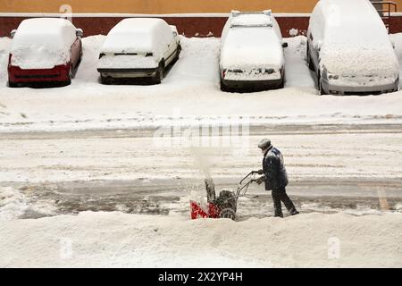 Der Mensch reinigt Schnee von der Straße mit einem Handschneegebläse Stockfoto