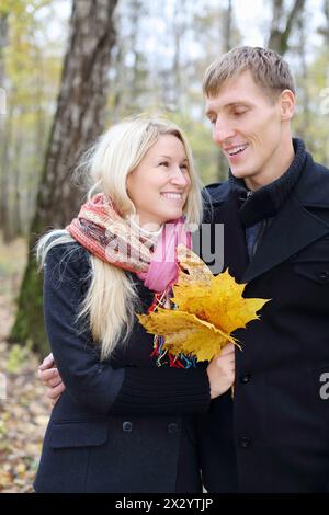 Glücklicher Mann und Frau mit gelbem Ahornblatt im Herbstwald. Geringe Schärfentiefe. Konzentrieren Sie sich auf den Menschen. Stockfoto