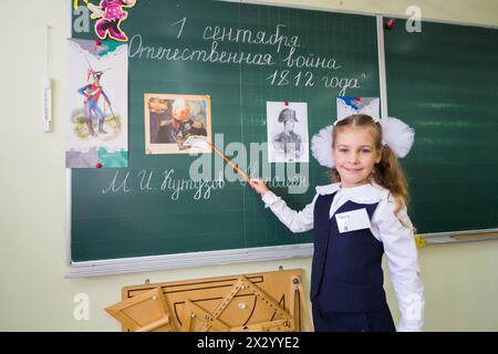 MOSKAU - SEP 1: Das kleine Schulmädchen Anya 7 Jahre alt steht am ersten Schultag im September mit einem Zeiger an der Tafel in der Schule Nr. 1349 Stockfoto