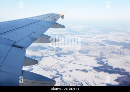 Flügel des Flugzeugs und Blick von oben auf schneebedeckte kleine Stadt, Straße und Felder. Stockfoto