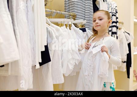 Das kleine Mädchen probiert weiße Bluse im Bekleidungsgeschäft an Stockfoto