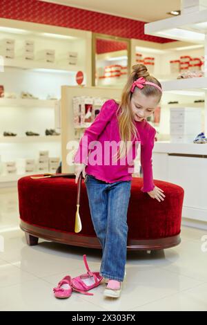 Das kleine Mädchen probiert einen neuen Schuh an, wobei es die Zunge des Fleißes im Laden ausdrückt Stockfoto