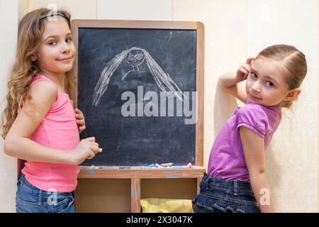 Zwei kleine Mädchen zeichnen mit Kreide an der Tafel, konzentrieren sich auf das linke Mädchen Stockfoto