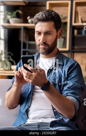 Kaukasischer Mann mit Handy-Anwendung auf dem Sofa im Heimbüro sitzen Stockfoto