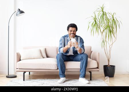 Mann lacht, während er zu Hause auf dem Smartphone SMS schreibt Stockfoto