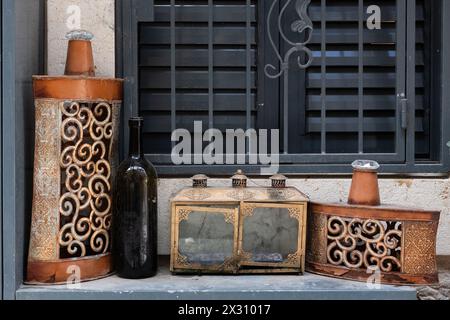 Ein kaputtes, schmutziges Glasgehäuse mit Messingtüren für eine Hanukkah Menora auf einer Fensterbank, zusammen mit einer Flasche und zwei abgenutzten Metallbehältern. Stockfoto
