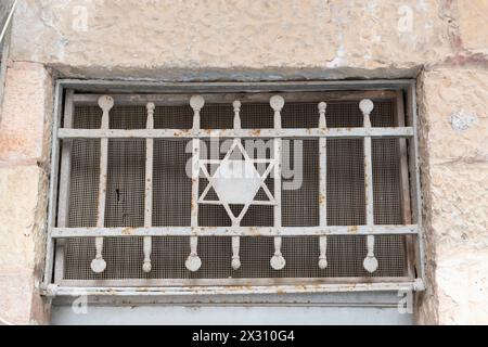 Ein kleines Fenster in einem alten Wohnhaus in Jerusalem im Stadtteil MEA She'arim mit einem Metallgitter und einer jüdischen David-St AR. Stockfoto