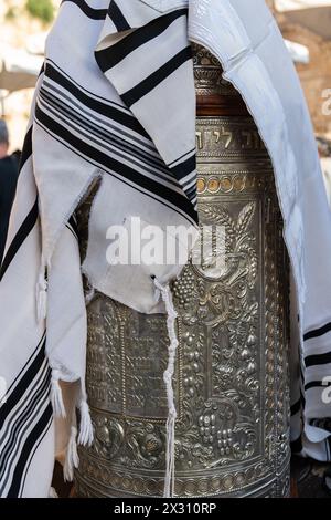 Ein Tallit- oder jüdischer Gebetschal mit geknüpften Fransen über einem silbernen Gehäuse, das eine Sefardi-Thora-Schriftrolle umschließt. Stockfoto