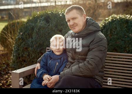 Herbstliche Familienzusammenhänge: Vater, 40 Jahre alt, und Sohn - wunderschöner 8-jähriger Junge, im Park sitzend. Stockfoto