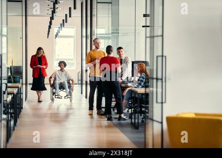 Eine vielfältige Gruppe junger Berufstätiger, darunter Geschäftsfrauen und ein afroamerikanischer Unternehmer im Rollstuhl, arbeiten zusammen Stockfoto