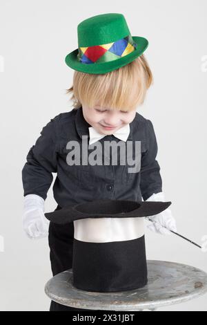 Ein kleiner Junge mit grünem Hut und magischem Zauberstab schaut in den Zylinder auf dem Tisch Stockfoto