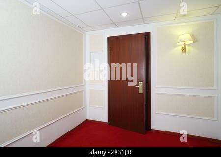 Offene Holztür, roter Teppich auf dem Boden und Lichter an der Wand im Hotel. Stockfoto