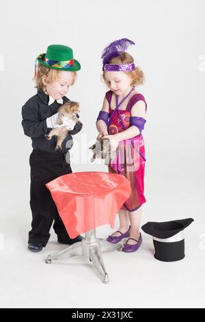 Kleine Junge und Mädchen in Kostümen, Magier halten Kätzchen neben einem kleinen runden Tisch Stockfoto