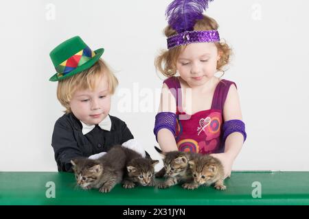 Kleiner Junge und Mädchen in Kostümen Zauberer und vier Kätzchen auf dem grünen Tisch Stockfoto