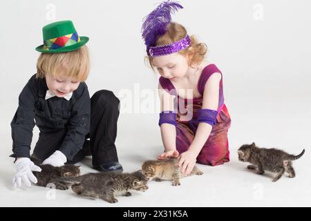 Zwei Kinder in Kostümen, Zauberer, die mit Kätzchen auf dem Boden spielen Stockfoto