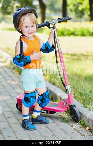 Kleiner Junge in Schutzausrüstung mit Elektroroller im Park Stockfoto