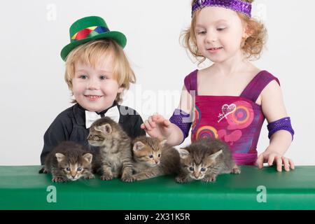 Kleiner Junge und Mädchen in Kostümen Zauberer und vier Kätzchen auf dem grünen Tisch Stockfoto