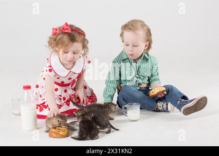 Kleine Mädchen und Junge trinken Milch, essen Brötchen und füttern die Kätzchen mit Milch Stockfoto