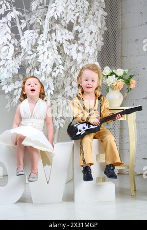 Ein kleines Mädchen in weißem Kleid und Popmusiker mit Gitarre sitzen auf Briefen und singen ein Lied Stockfoto