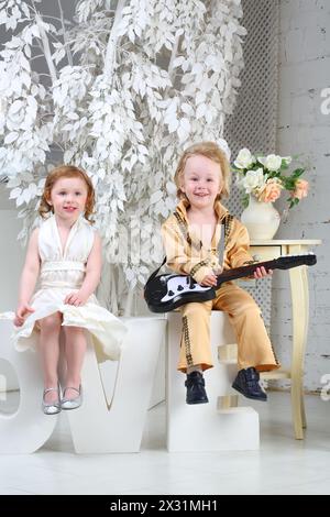 Ein kleines Mädchen in weißem Kleid und Popmusiker mit Gitarre sitzen auf Briefen Love Stockfoto