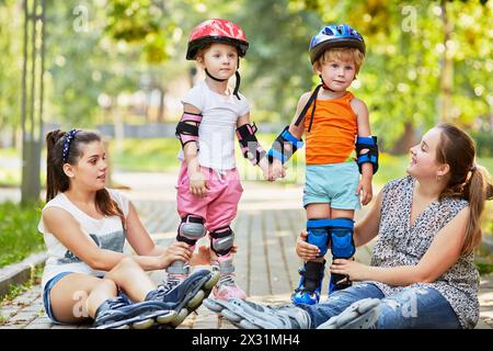 Zwei Mädchen sitzen auf dem Boden und unterstützen Kinder in Rollen, die Hände halten Stockfoto