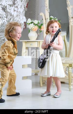 Kleine Kinder im Pop-Retro-Anzug lachen und spielen Gitarre Stockfoto