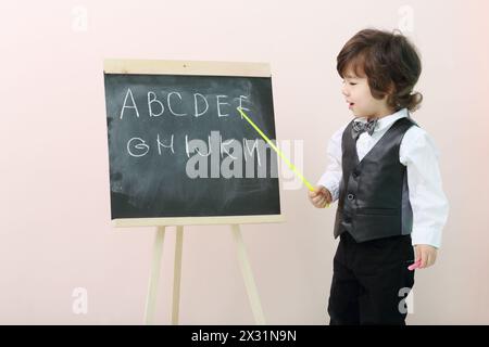 Der kleine Junge zeigt mit Zeigerbriefen an der Tafel und spricht im Studio. Stockfoto