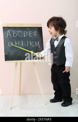 Der kleine Junge zeigt mit gelben Zeigerbuchstaben an der Tafel und nennt es im Studio. Stockfoto