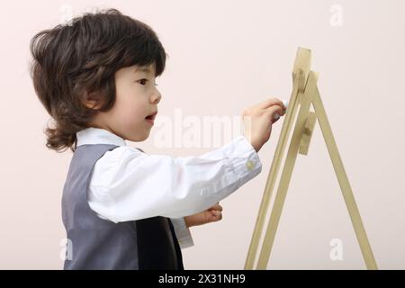 Der kleine süße, konzentrierte Junge zeichnet mit Kreide an der Tafel im Studio. Stockfoto