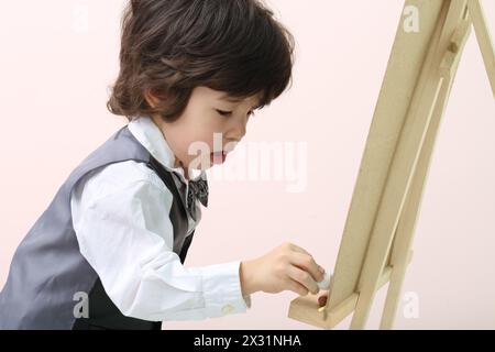 Der kleine brünette Junge zeichnet mit Kreide an der Tafel im Studio. Stockfoto