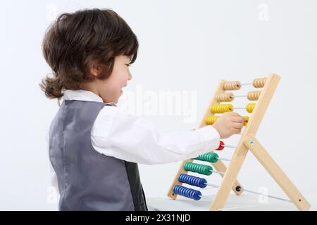 Kleiner glücklicher Junge in Weste spielt mit farbenfrohen Abacus im weißen Studio. Stockfoto