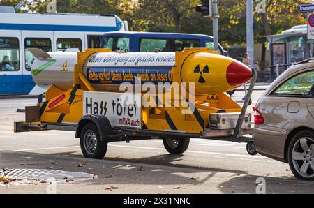 Auf einem Anhänger hinter einem Auto ist symbolisch eine Atombombe zu sehne. Darauf steht, dass Hass tötet - mRNA auch. (Zürich, Schweiz, 29.10.2022) Stockfoto