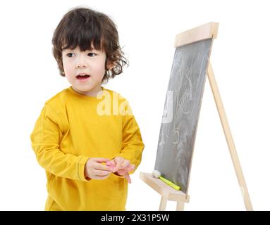 Kleiner Junge mit Kreide steht in der Nähe der Tafel, isoliert auf weißem Hintergrund. Stockfoto