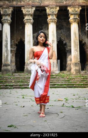 Porträt einer wunderschönen bengalischen Frau in rot-weißen traditionellen ethnischen Saree und Schmuck vor einem historischen Gebäude in Kalkutta, Indien, am März Stockfoto