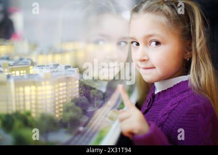 Das kleine Mädchen zeigt auf die Grundrisse von Wohngebäuden. Geringe Schärfentiefe. Stockfoto