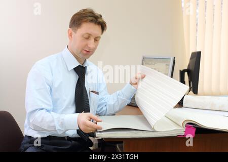 Ein Mann mit Krawatte sitzt im Büro eines Maklers und sieht sich Tapeten an. Stockfoto