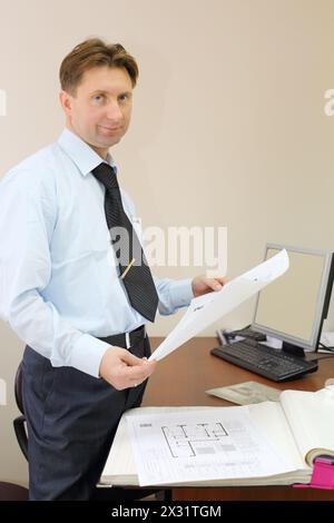 Ein Mann mit weißem Hemd hält Zeichnungen von der Wohnung im Büro des Maklers. Stockfoto