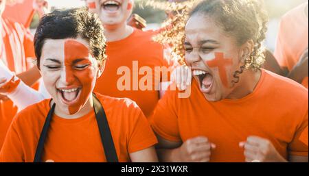 Orange Sportfans, die Spaß haben, ihre Mannschaft zu unterstützen - Fußballfans, die Spaß bei der Wettkampfveranstaltung haben - konzentrieren sich auf das afrikanische Mädchen-Gesicht Stockfoto