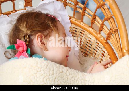 Das kleine schöne Mädchen liegt unter der Decke in einem großen Korb. Stockfoto