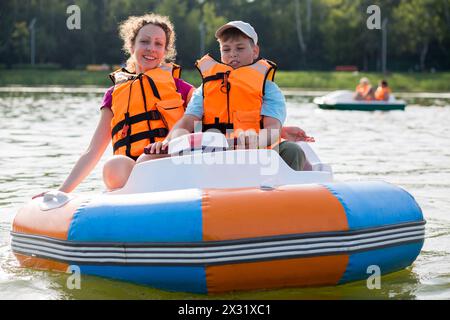 Sohn und Mutter in Schwimmwesten, die in einem Gummiboot mit elektrischem Rad den Fluss hinunterschweben Stockfoto