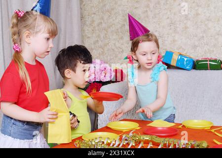 Kleine süße Kinder in Mützen servierten roten Tisch auf der Geburtstagsfeier. Stockfoto