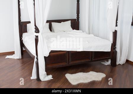 Hölzernes Himmelbett und ein weißes Fell auf dem Boden in einem hellen Raum Stockfoto