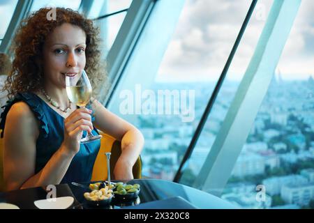 Schöne Frau trinkt Wein im Restaurant, die Stadt ist durch das Fenster zu sehen. Stockfoto