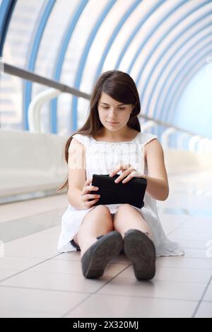 Hübsches Mädchen in weißer Bluse hält den Tablet-pc in einer hellen, langen Galerie. Stockfoto