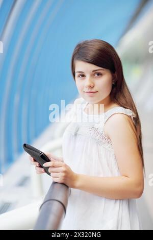 Hübsches Mädchen in weißer Bluse mit Tablet-pc schaut in die Kamera in der Lichtgalerie. Stockfoto