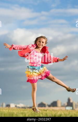 Kleines Mädchen, das Spaß hat und im Gras auf einem Hintergrund der städtischen Landschaft springt Stockfoto