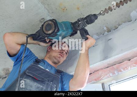 Der Arbeiter in Arbeitskleidung, der mit einem großen Perforator arbeitet Stockfoto